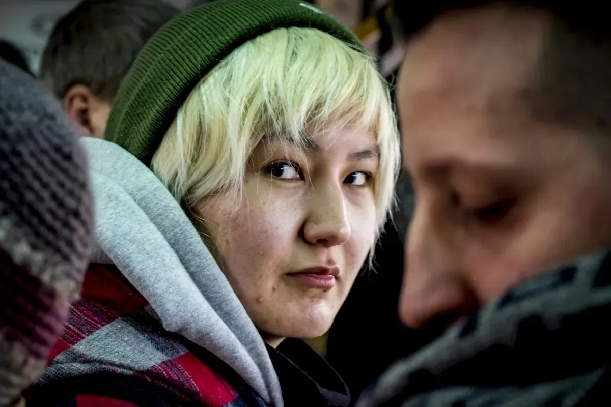 Short-haired person in a green beanie looking sideways in a crowd